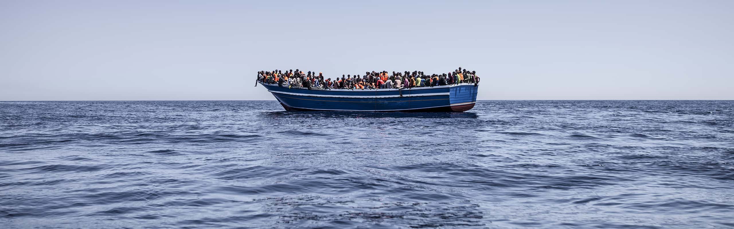 Een eenvoudige boot vol met vluchtelngen, drijvend op open zee